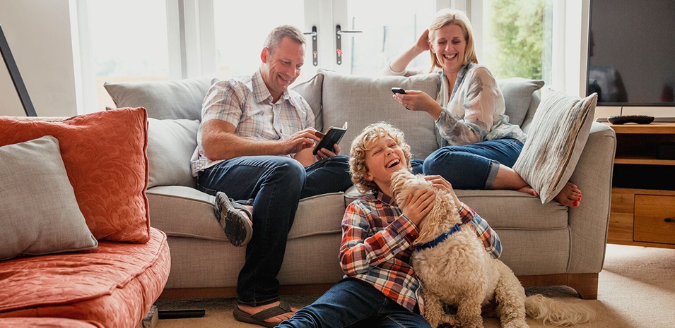 Una familia feliz sentada en la sala de estar. Su hijo está sentado en el piso con el perro de la familia lamiéndole la cara.