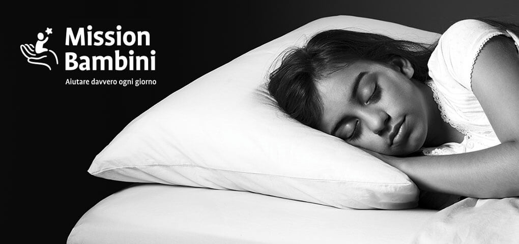 Una niña dormida en la cama. Esta imagen tiene el logotipo de Mission Bambini.